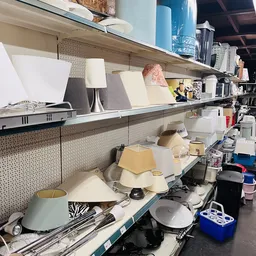 Stellingen met diverse huishoudelijke artikelen zoals lampen, servies en keukengerei in een kringloopwinkel