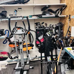 Stellingen met tweedehands sportartikelen en fietsonderdelen, waaronder hometrainers, golfclubs en fietsen