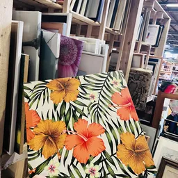 Close-up van een kussen of textiel met hibiscusbloemen in oranje en geel op zwarte bladmotief