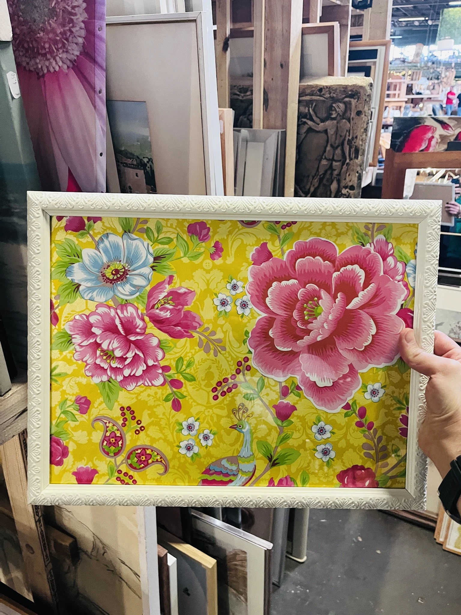Ingelijste textielprint met geel patroon en roze bloemen, gehouden in een hand