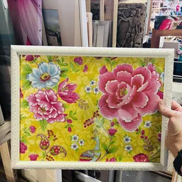 Ingelijste textielprint met geel patroon en roze bloemen, gehouden in een hand