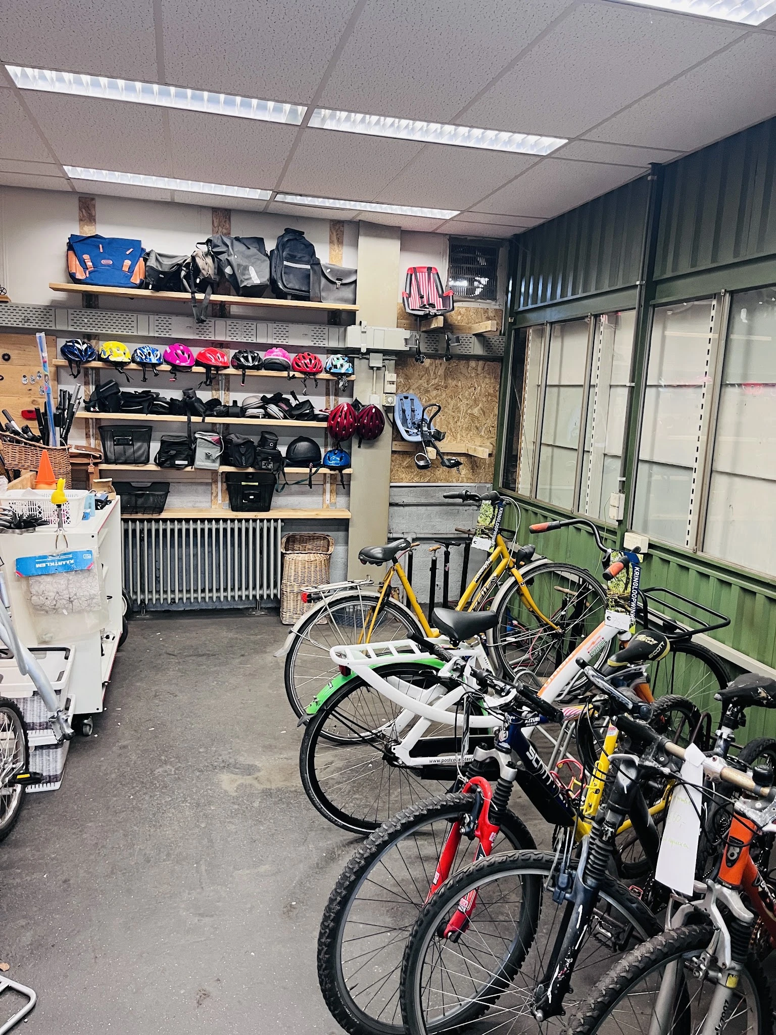 Binnenaanzicht kringloopwinkel met fietsen op de voorgrond en stellingen met sportartikelen, helmen en tassen op de muur