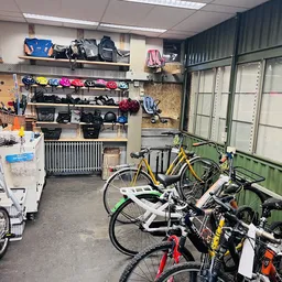 Binnenaanzicht kringloopwinkel met fietsen op de voorgrond en stellingen met sportartikelen, helmen en tassen op de muur