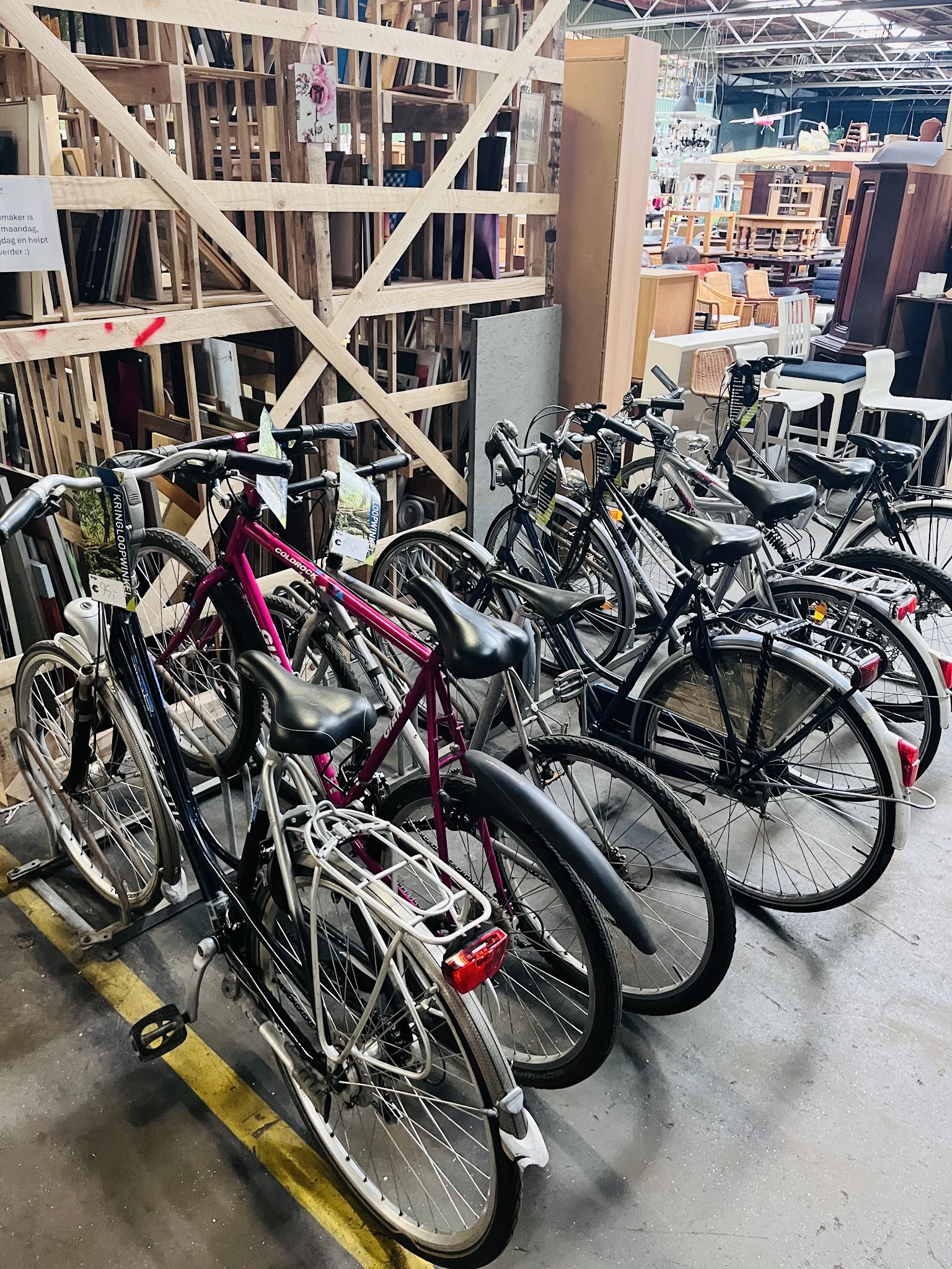 Rekken met tweedehands fietsen in verschillende kleuren, waaronder een roze fiets op de voorgrond