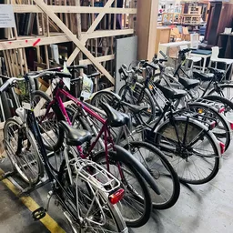 Rekken met tweedehands fietsen in verschillende kleuren, waaronder een roze fiets op de voorgrond