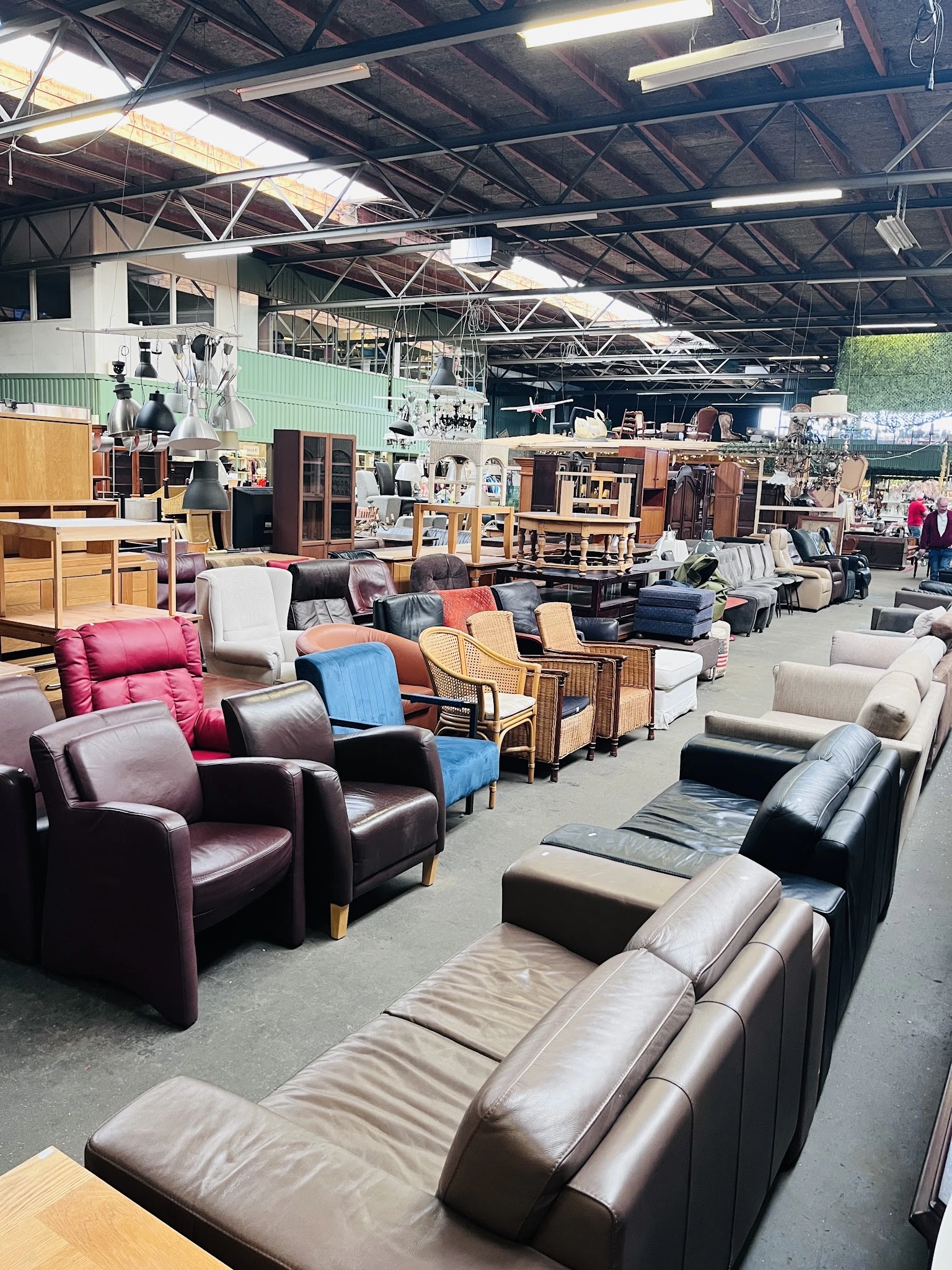 Magazijnhal vol met tweedehands meubels: fauteuils, stoelen, kasten en tafels in verschillende stijlen en kleuren