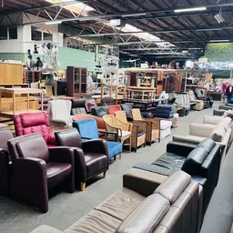 Magazijnhal vol met tweedehands meubels: fauteuils, stoelen, kasten en tafels in verschillende stijlen en kleuren
