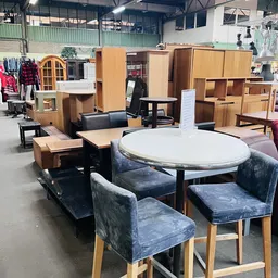 Ronde witte tafel met grijze stoelen en houten meubels op display in kringloopwinkel