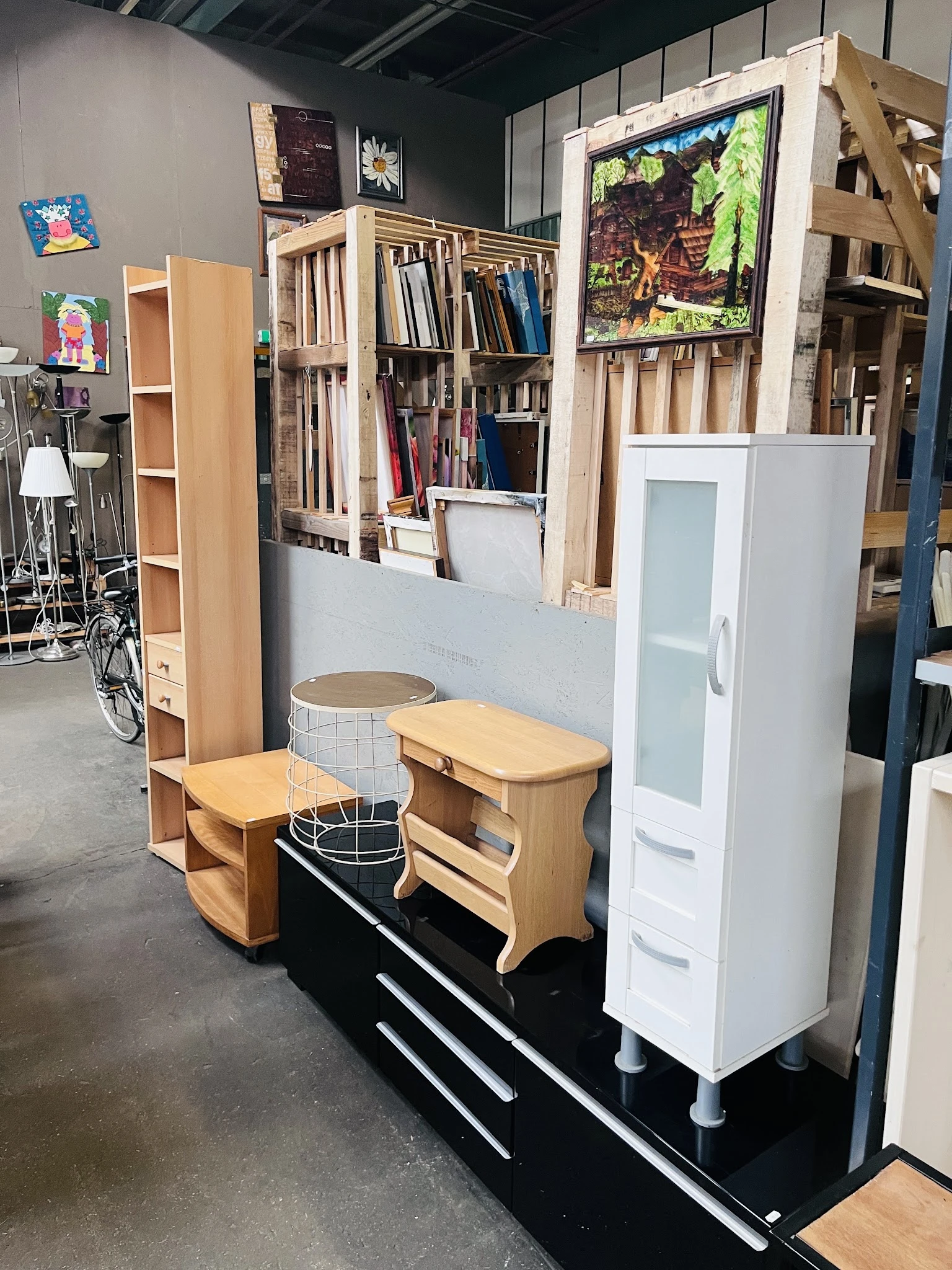 Uitgestalde meubels in de kringloopwinkel: houten bankjes, witte kasten en verschillende huisraadstukken.