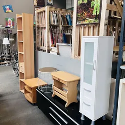 Uitgestalde meubels in de kringloopwinkel: houten bankjes, witte kasten en verschillende huisraadstukken.