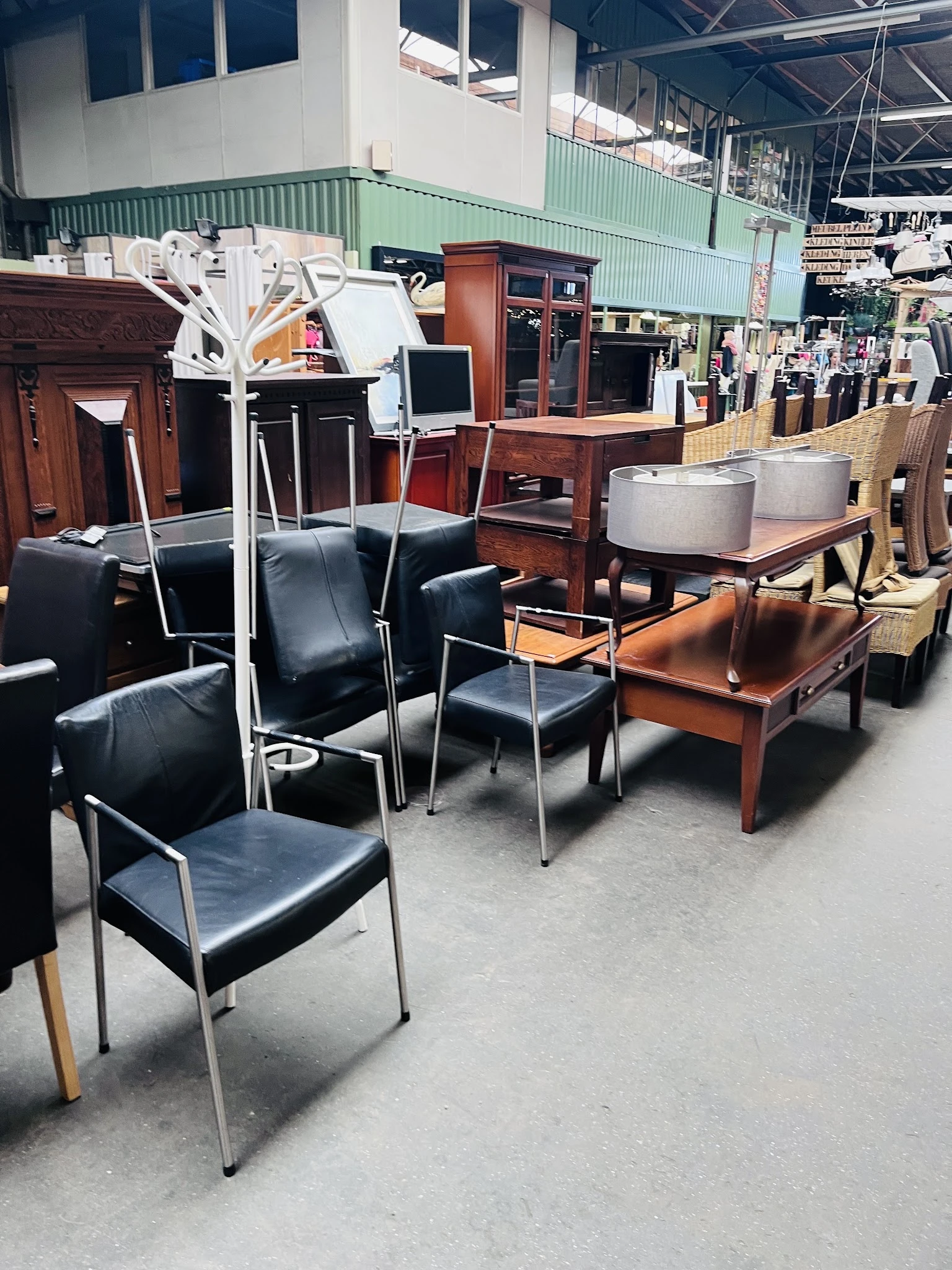 Diverse meubels uitgestald in kringloopwinkel: zwarte stoelen, houten tafels en kastjes