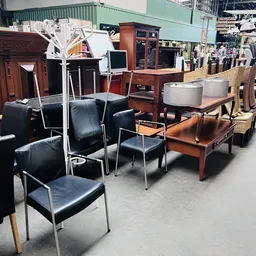 Diverse meubels uitgestald in kringloopwinkel: zwarte stoelen, houten tafels en kastjes