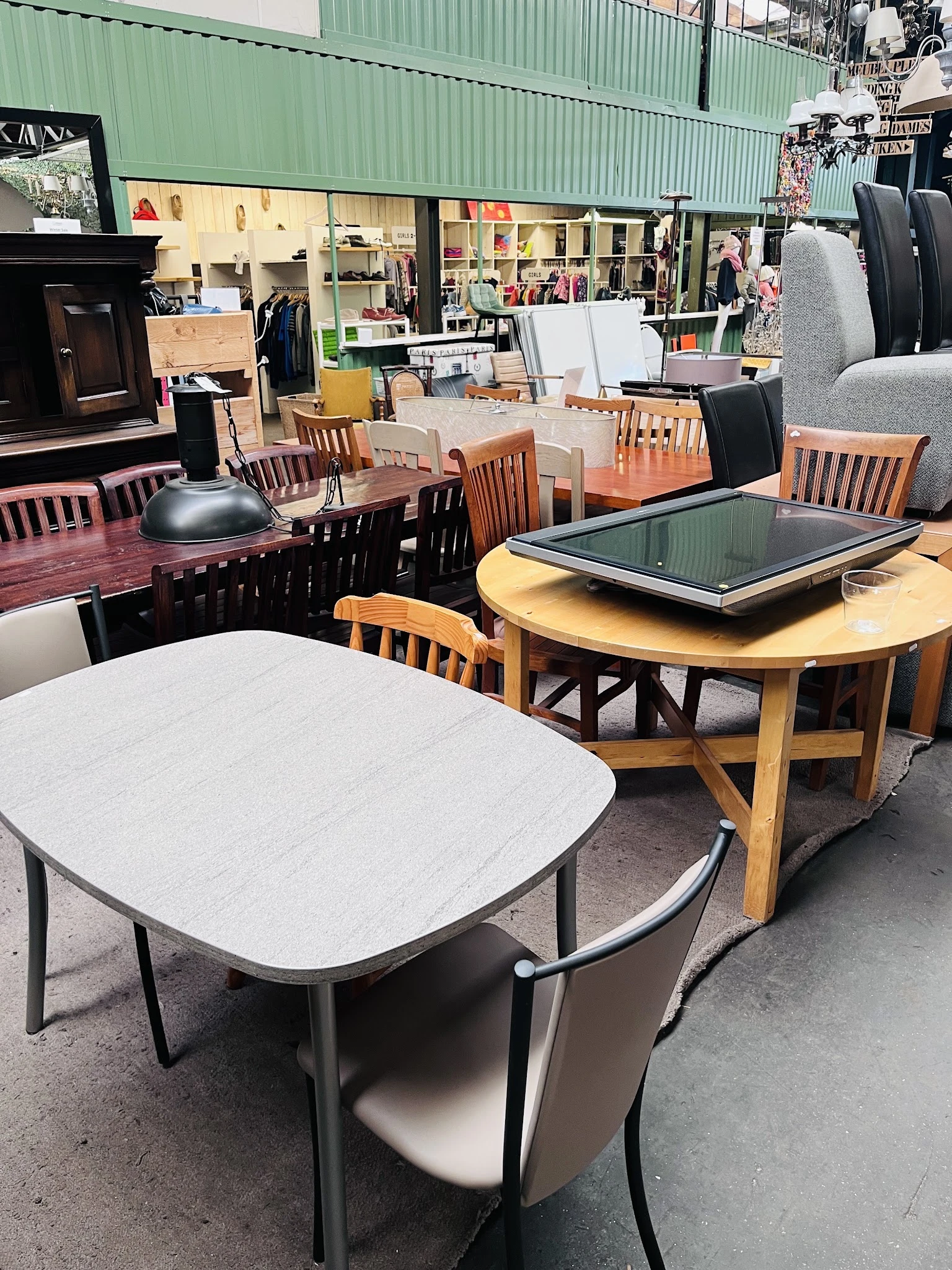 Diverse tweedehands meubels: witte en houten eetkamertafels met stoelen, lampen en kasten op display