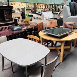 Diverse tweedehands meubels: witte en houten eetkamertafels met stoelen, lampen en kasten op display