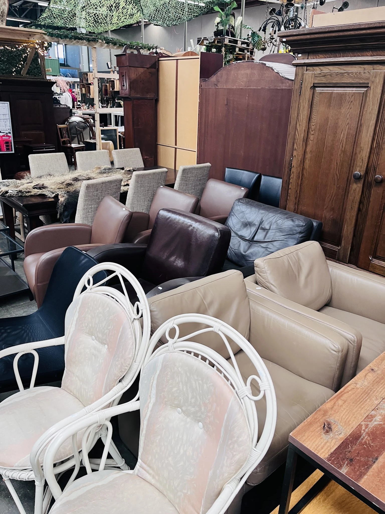 Uitgestalde meubels: eetkamerstoelen met witte frame en beige/roze bekleding, en bruine/zwarte leren zitmeubels op de achterg
