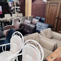 Uitgestalde meubels: eetkamerstoelen met witte frame en beige/roze bekleding, en bruine/zwarte leren zitmeubels op de achterg