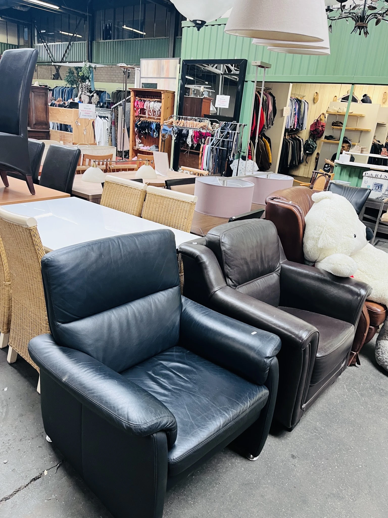 Zwartlederen fauteuils en stoelen in de winkel, met op de achtergrond kleding op hangers en ander meubilair