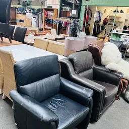 Zwartlederen fauteuils en stoelen in de winkel, met op de achtergrond kleding op hangers en ander meubilair