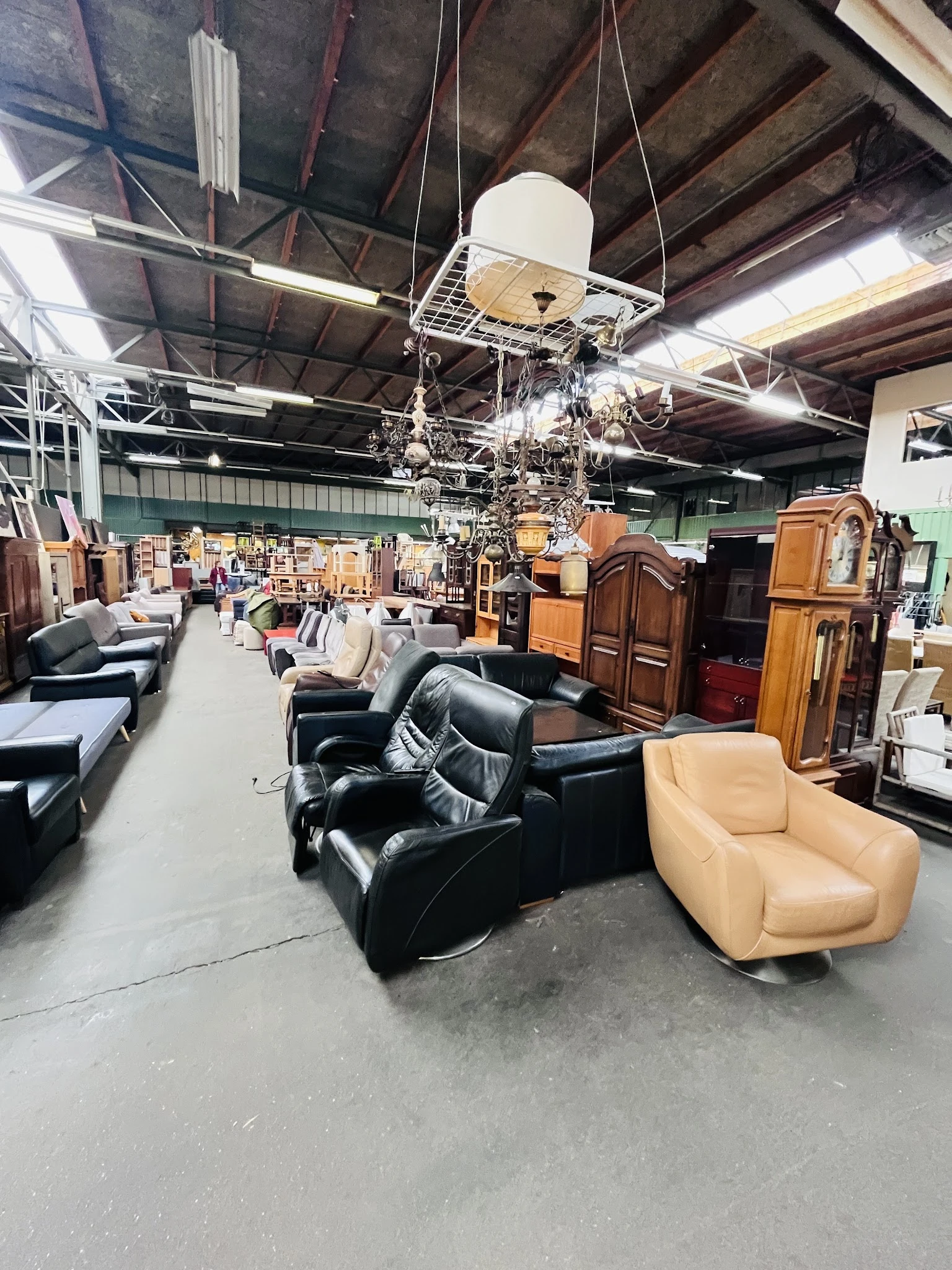 Winkelhal met diverse meubels uitgestald: zwarte leren fauteuils, beige stoelen, houten kasten en kroonluchters hangend van h
