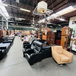 Winkelhal met diverse meubels uitgestald: zwarte leren fauteuils, beige stoelen, houten kasten en kroonluchters hangend van h