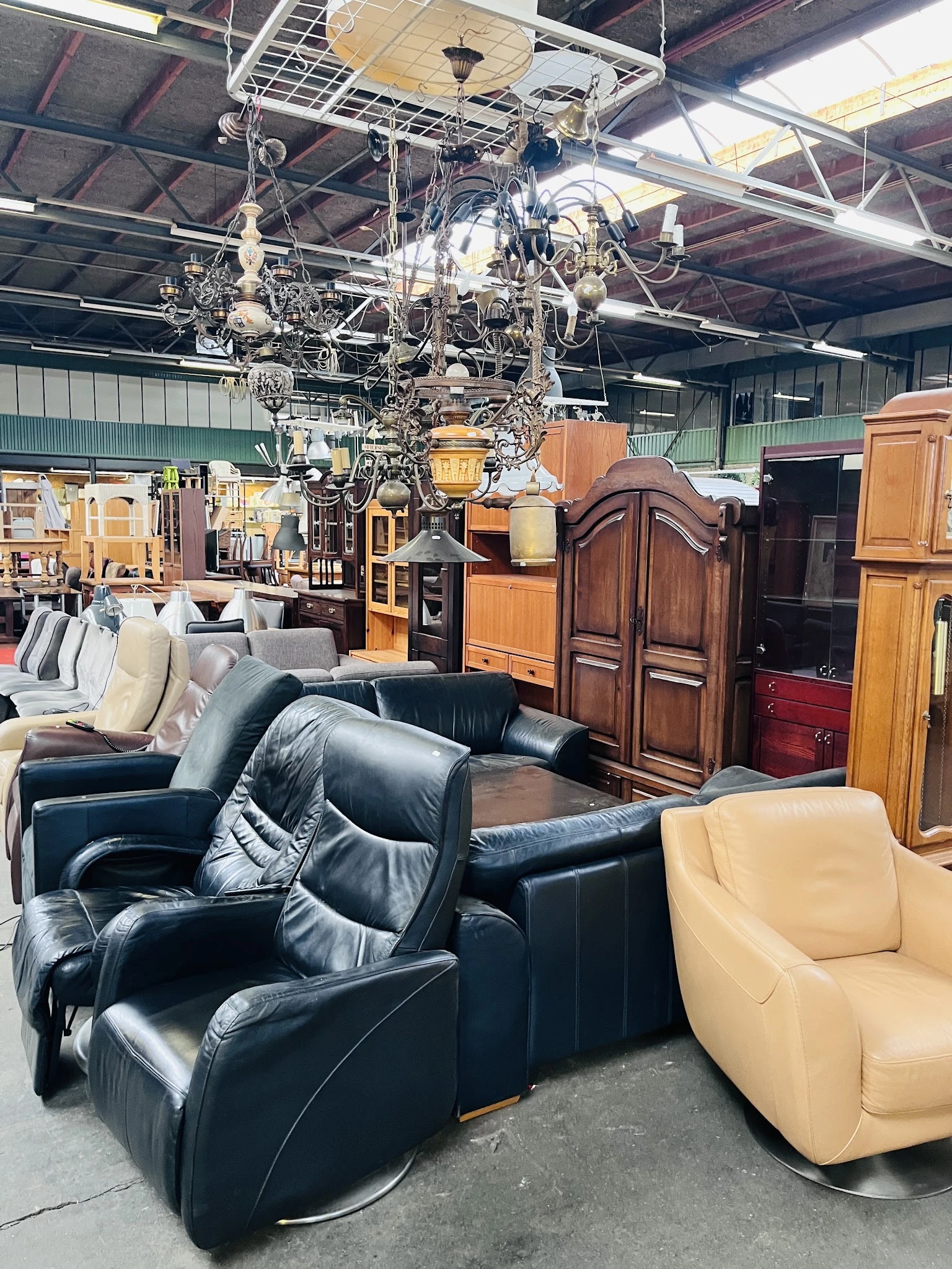 Uitgestalde meubels in kringloopwinkel: zwarte leren fauteuils, houten kasten en een crèmekleurige stoel op de winkelvloer