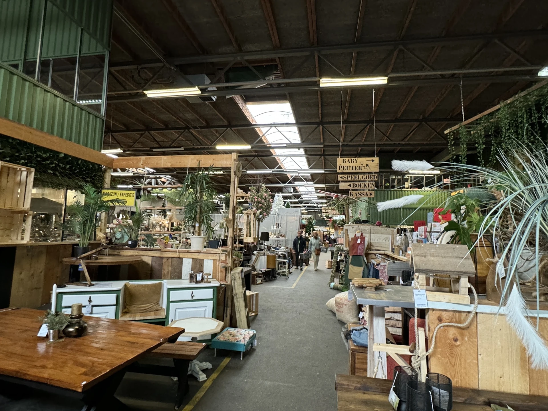 Binnenaanzicht van kringloopwinkel met stellingen, toonbanken, diverse artikelen en bezoekers op de vloer