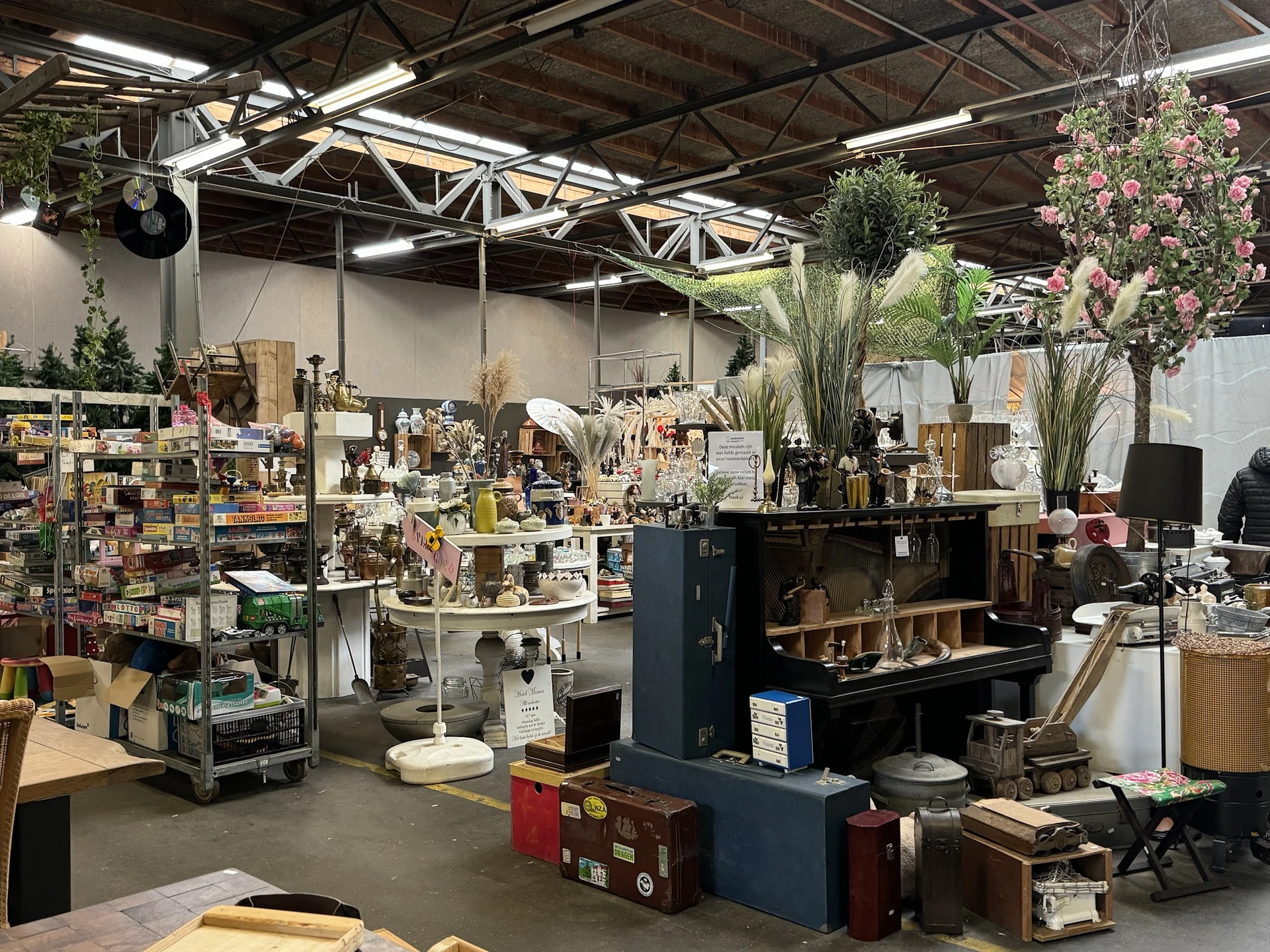 Winkelvloer van kringloopwinkel met diverse spullen, meubels, decoratie en bloemen in stellingen en op tafels