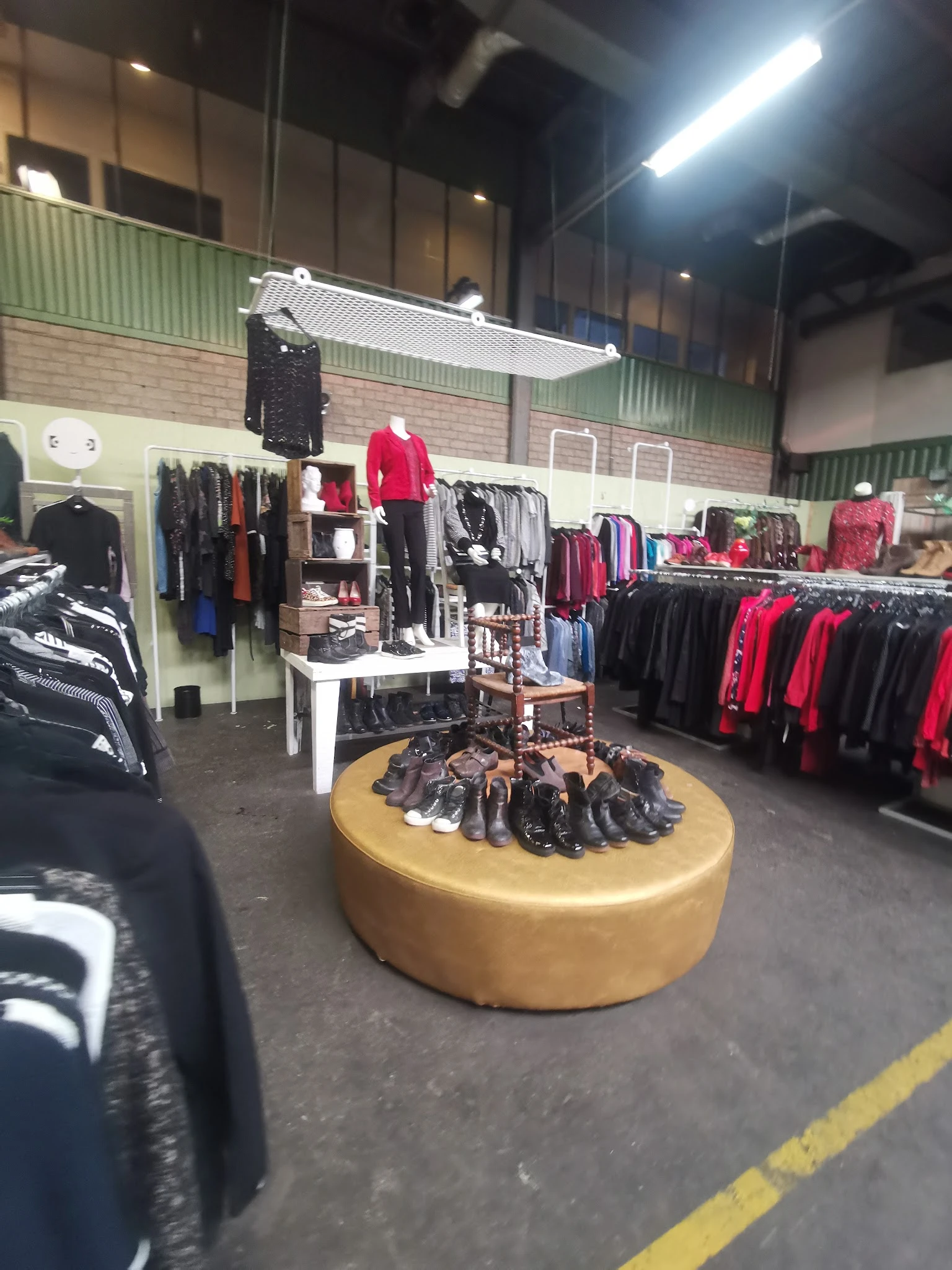 Winkelvloer met kledingrekken, een geel rond schoenenrek in het centrum en verschillende afdeling met zwarte en rode kleding