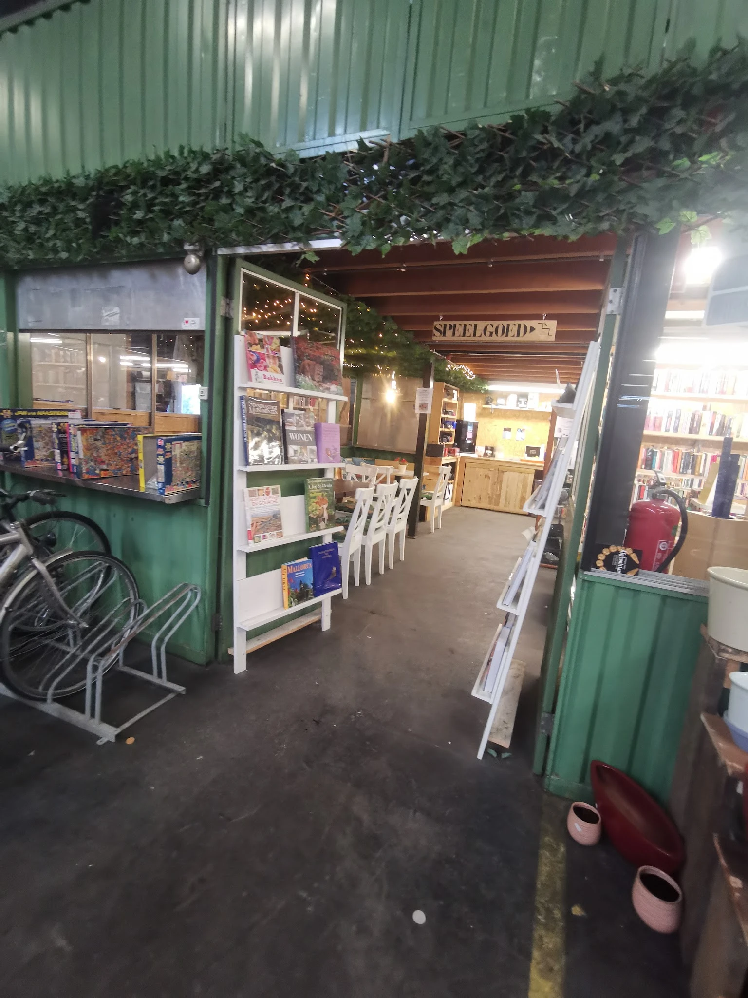 Winkelinterieur met groen gekleurde ingang, stellingen met boeken en spullen, witte stoelen, verlichting en groene planten