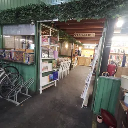 Winkelinterieur met groen gekleurde ingang, stellingen met boeken en spullen, witte stoelen, verlichting en groene planten