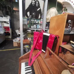 Roze handtas of reistas met zwarte details, uitgestald op houten meubel in kringloopwinkel