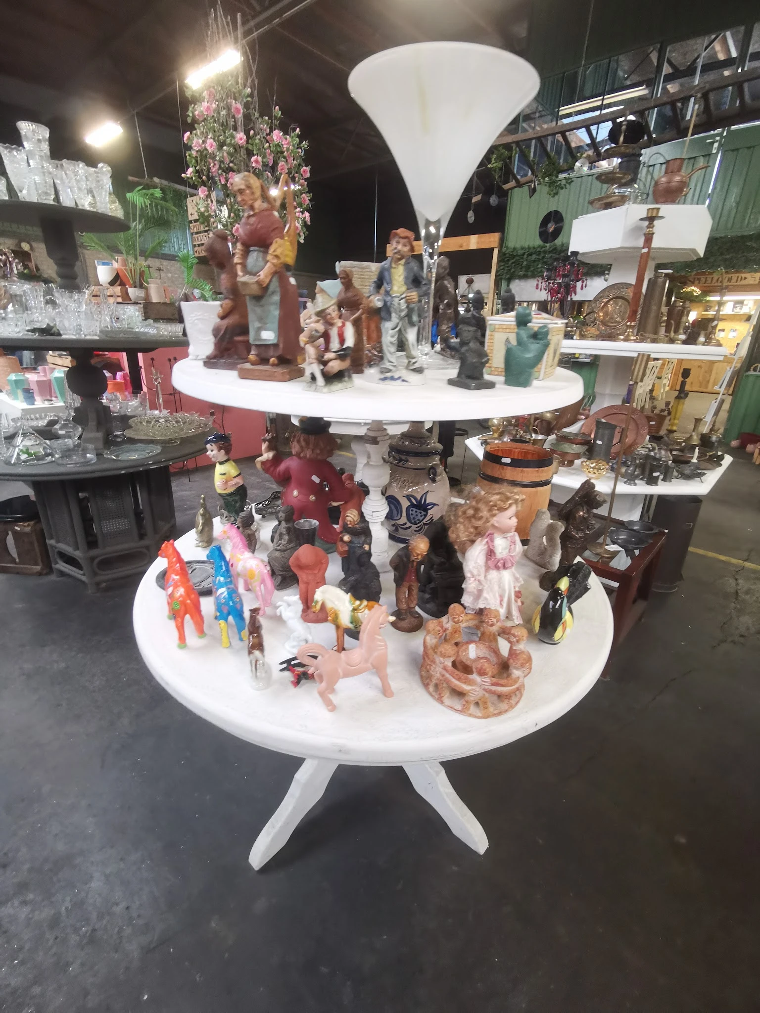 Twee witte ronde tafels vol met verzamelde beeldjes, speelgoed en decoratieve voorwerpen in verschillende stijlen en material