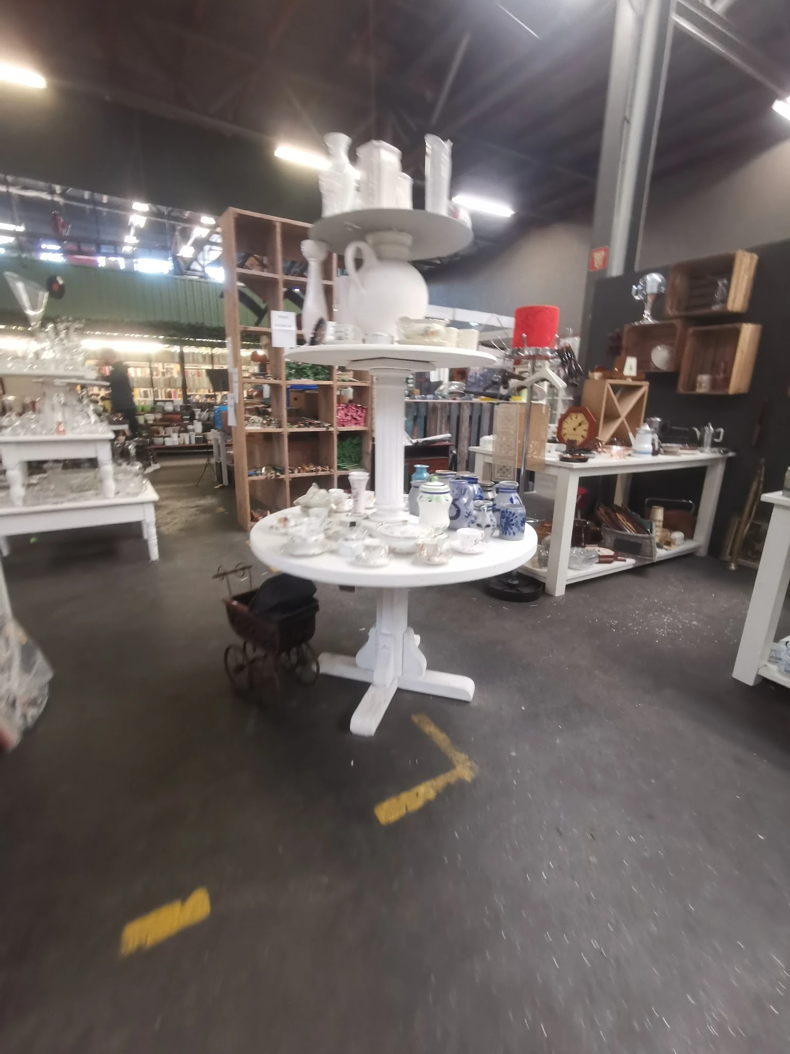 Winkelvloer van kringloopwinkel met witte ronde tafel, houten kasten, boekenrekken en diverse huishoudelijke items op display