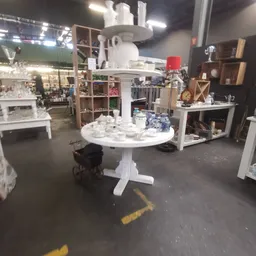 Winkelvloer van kringloopwinkel met witte ronde tafel, houten kasten, boekenrekken en diverse huishoudelijke items op display