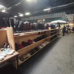 Winkelfloor met houten stellingen vol tweedehands kleding, neonverlichting, en klanten in de kringloopwinkel