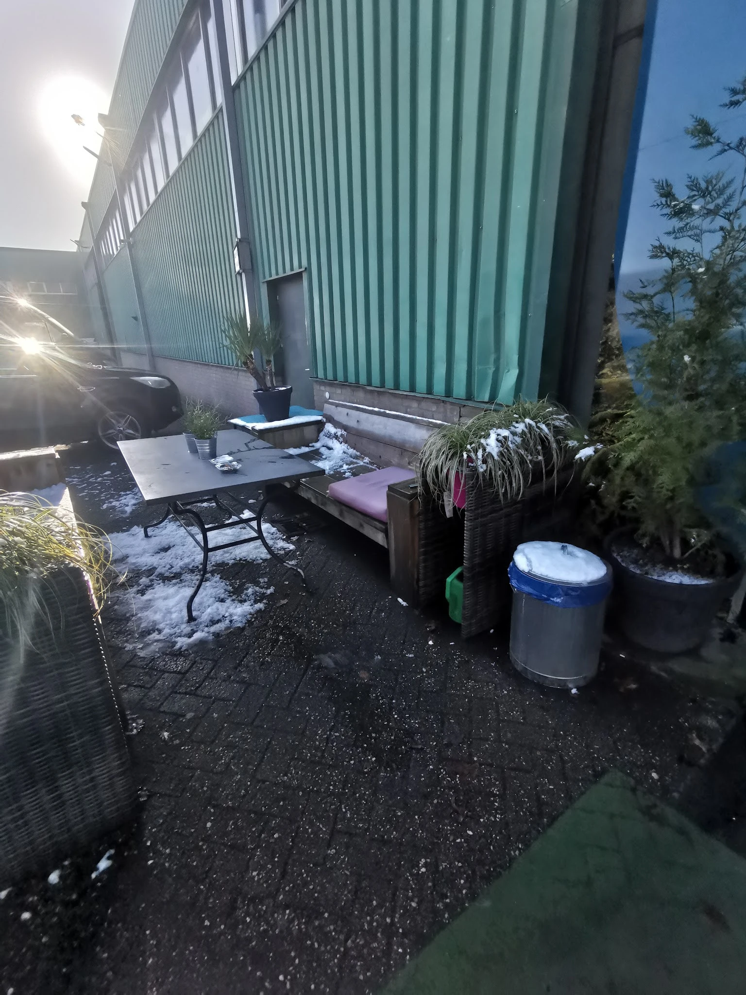 Buitenterras met tafel, bank en plantenbakken tegen een groene metalen wand