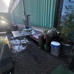 Buitenterras met tafel, bank en plantenbakken tegen een groene metalen wand