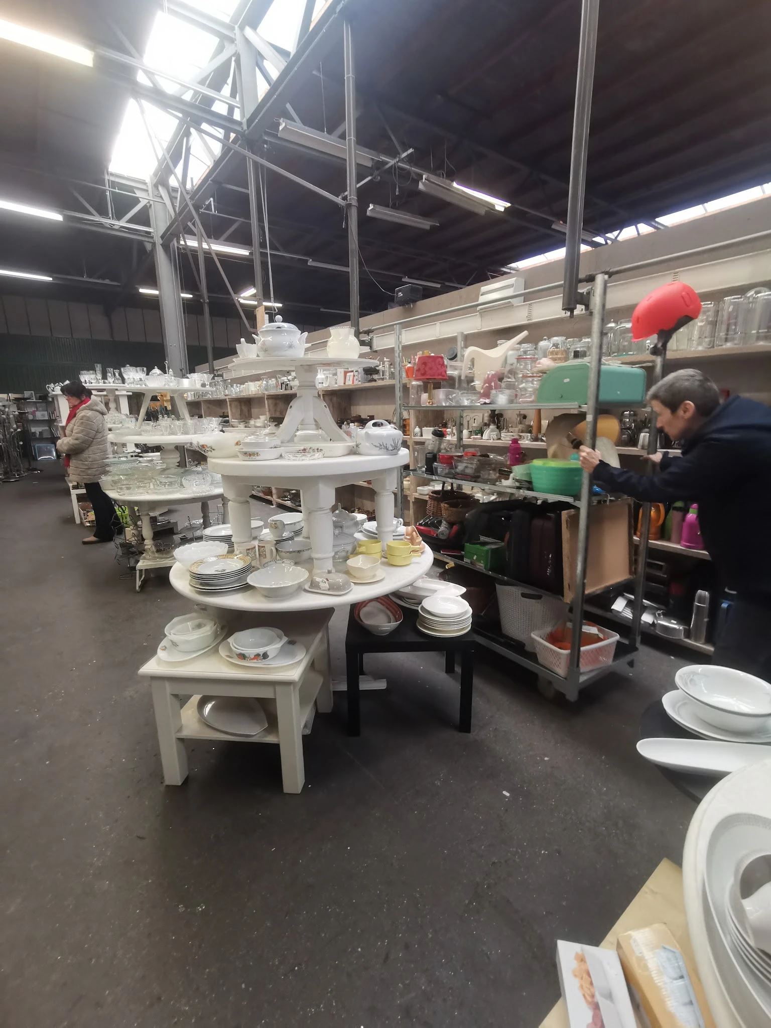 Uitgestalde serviesgoed en huishoudartikelen op witte tafels in de kringloopwinkel