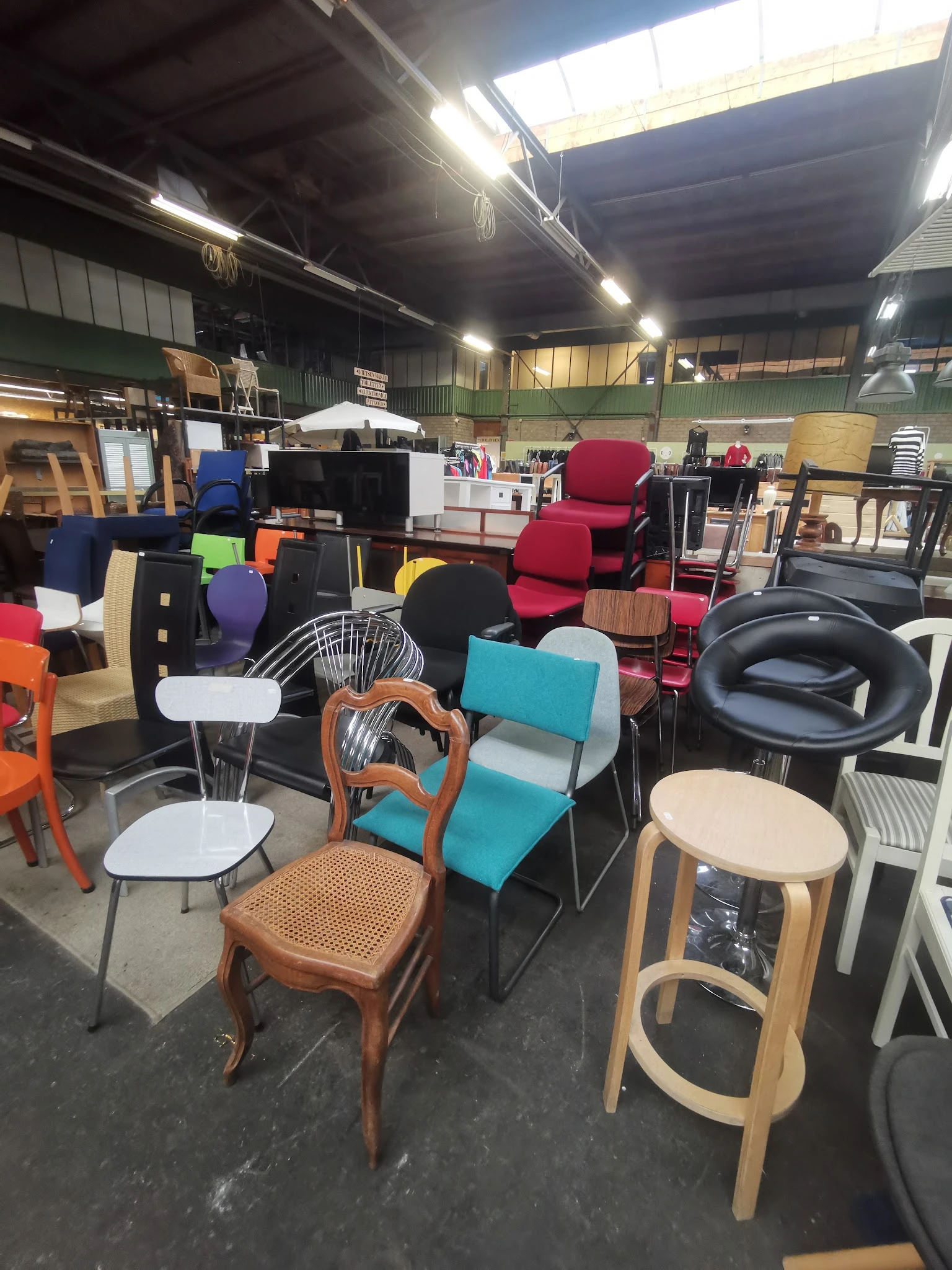 Diverse tweedehands stoelen en meubels in verschillende kleuren en stijlen uitgestald in een kringloopwinkel