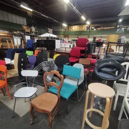 Diverse tweedehands stoelen en meubels in verschillende kleuren en stijlen uitgestald in een kringloopwinkel