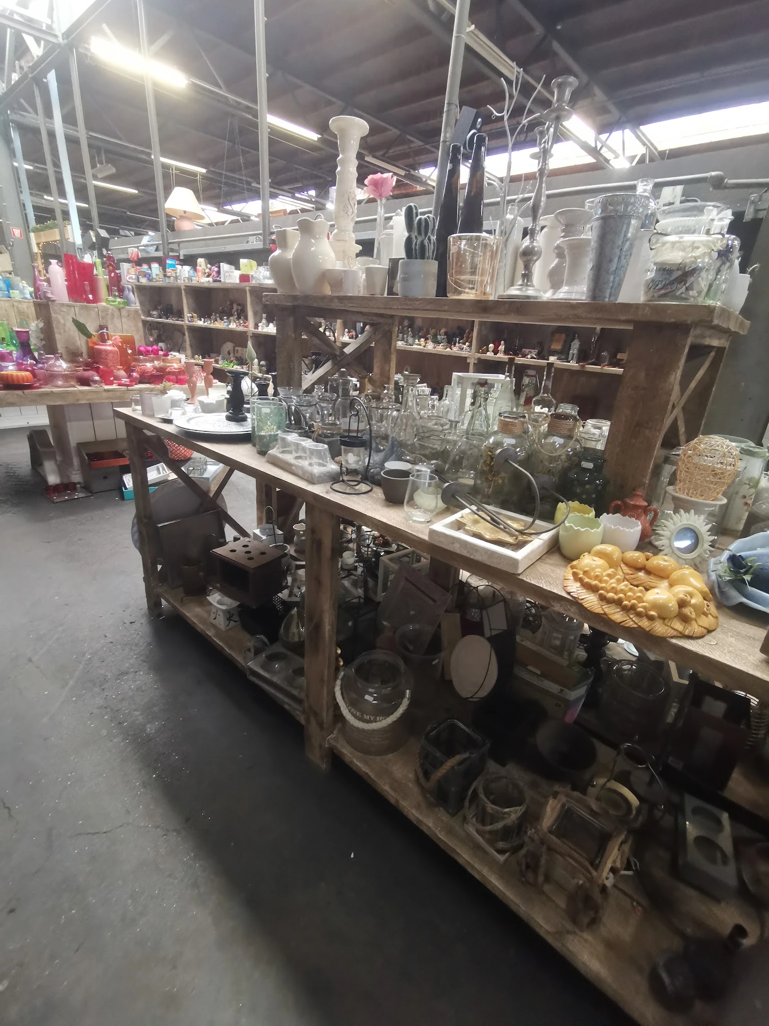 Werkbank met glaswerk, kruiken en serviesgoed in een kringloopwinkel, stellingen op de achtergrond
