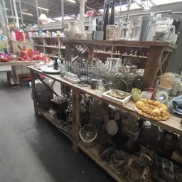 Werkbank met glaswerk, kruiken en serviesgoed in een kringloopwinkel, stellingen op de achtergrond