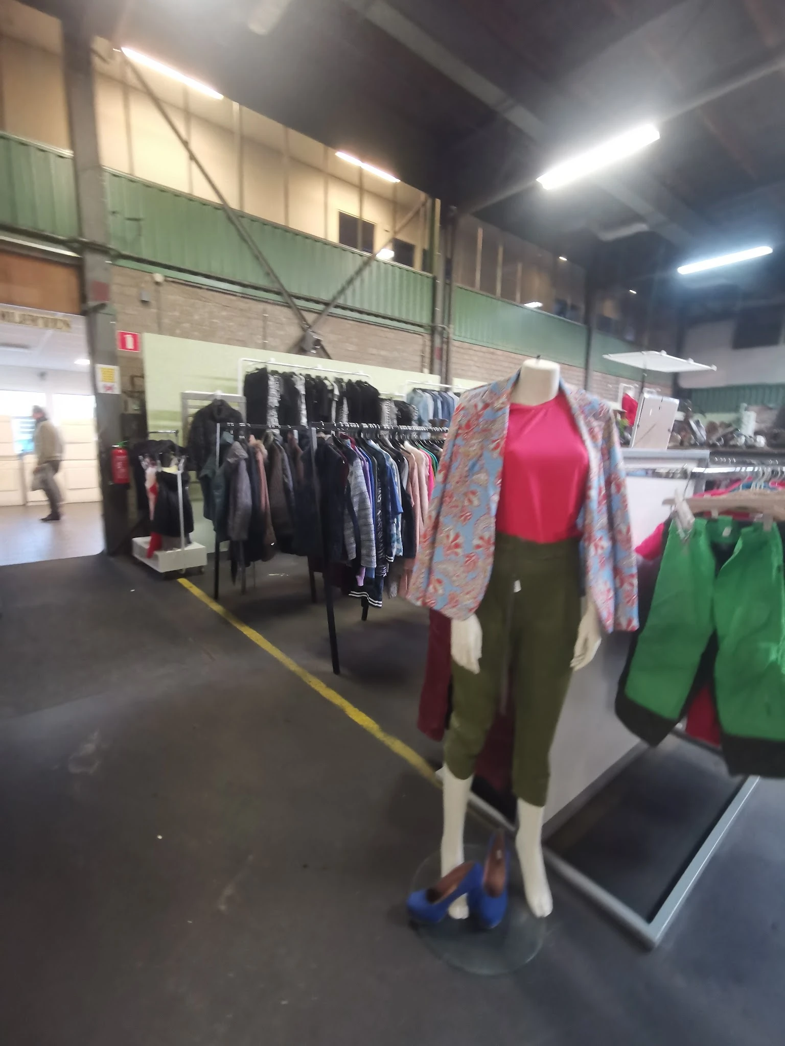 Rekken met tweedehands kleding, waaronder jasjes en broeken, met kledingpoppen die outfits presenteren