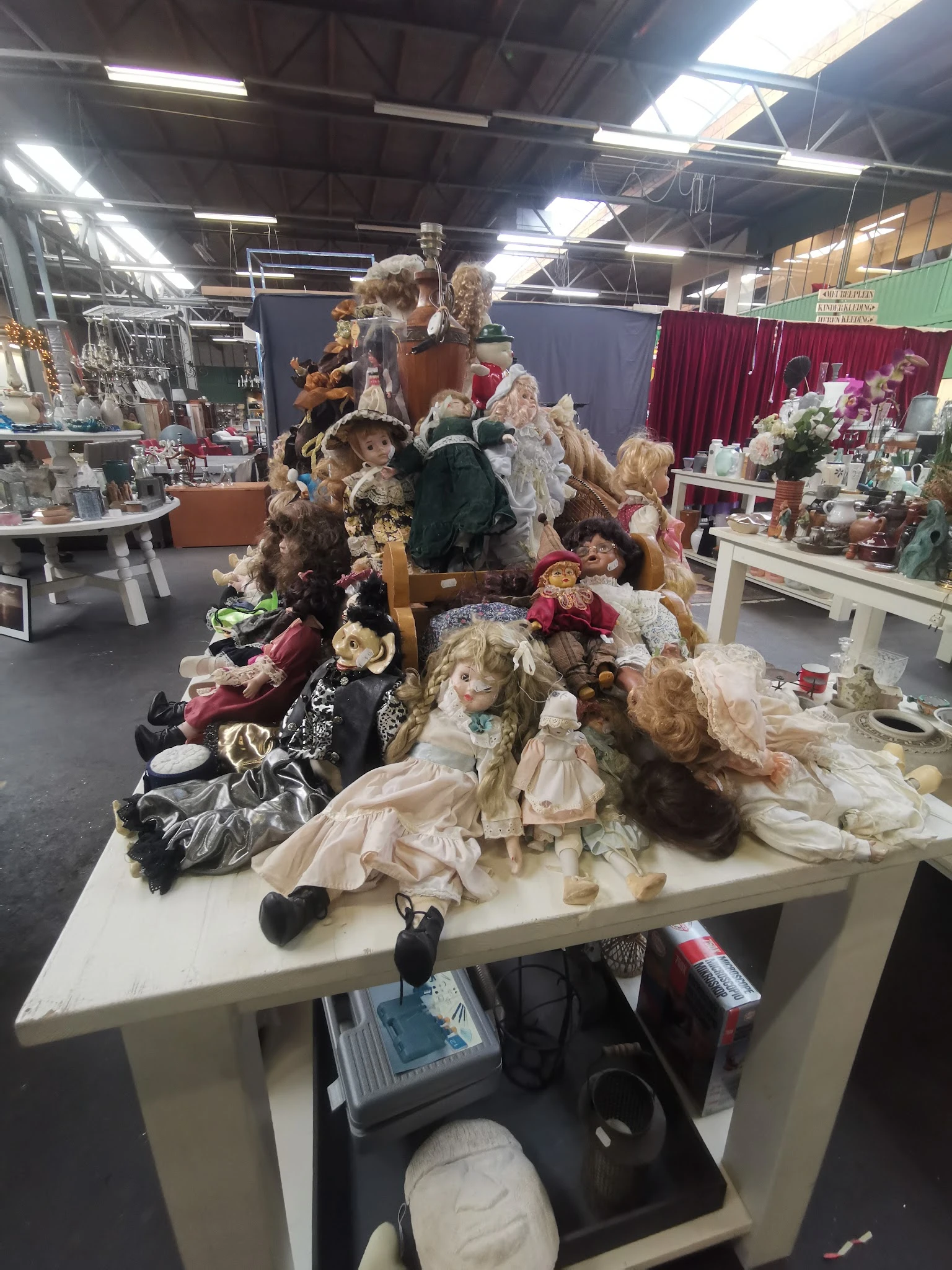 Collectie antieke poppen en poppenkleding uitgestald op een tafel in de winkel