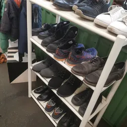 Wit metalen schoenenrek met diverse tweedehands schoenen en laarzen in verschillende kleuren