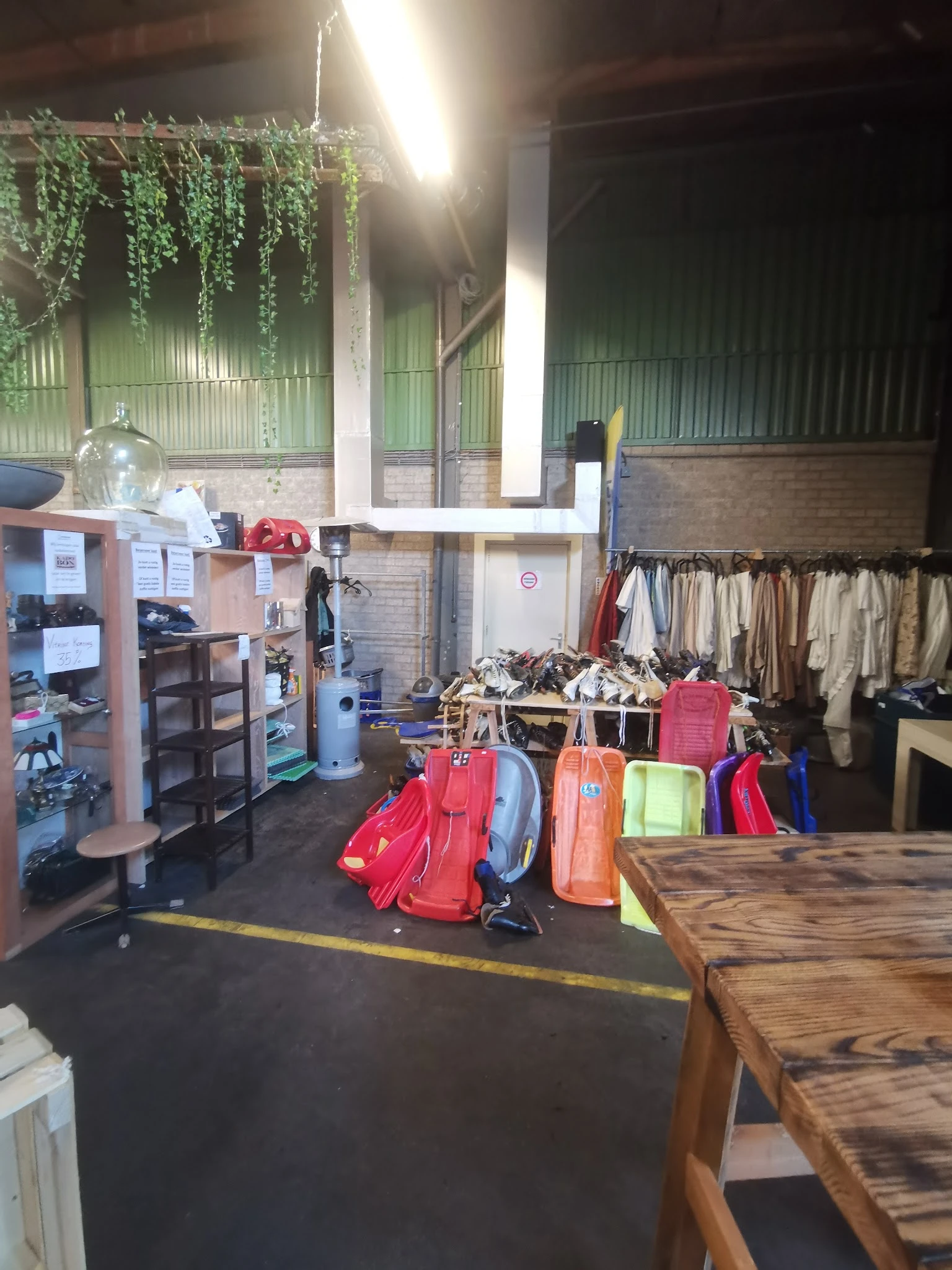 Rekken met tweedehands kleding en uitgestalde tassen en koffers in een kringloopwinkel