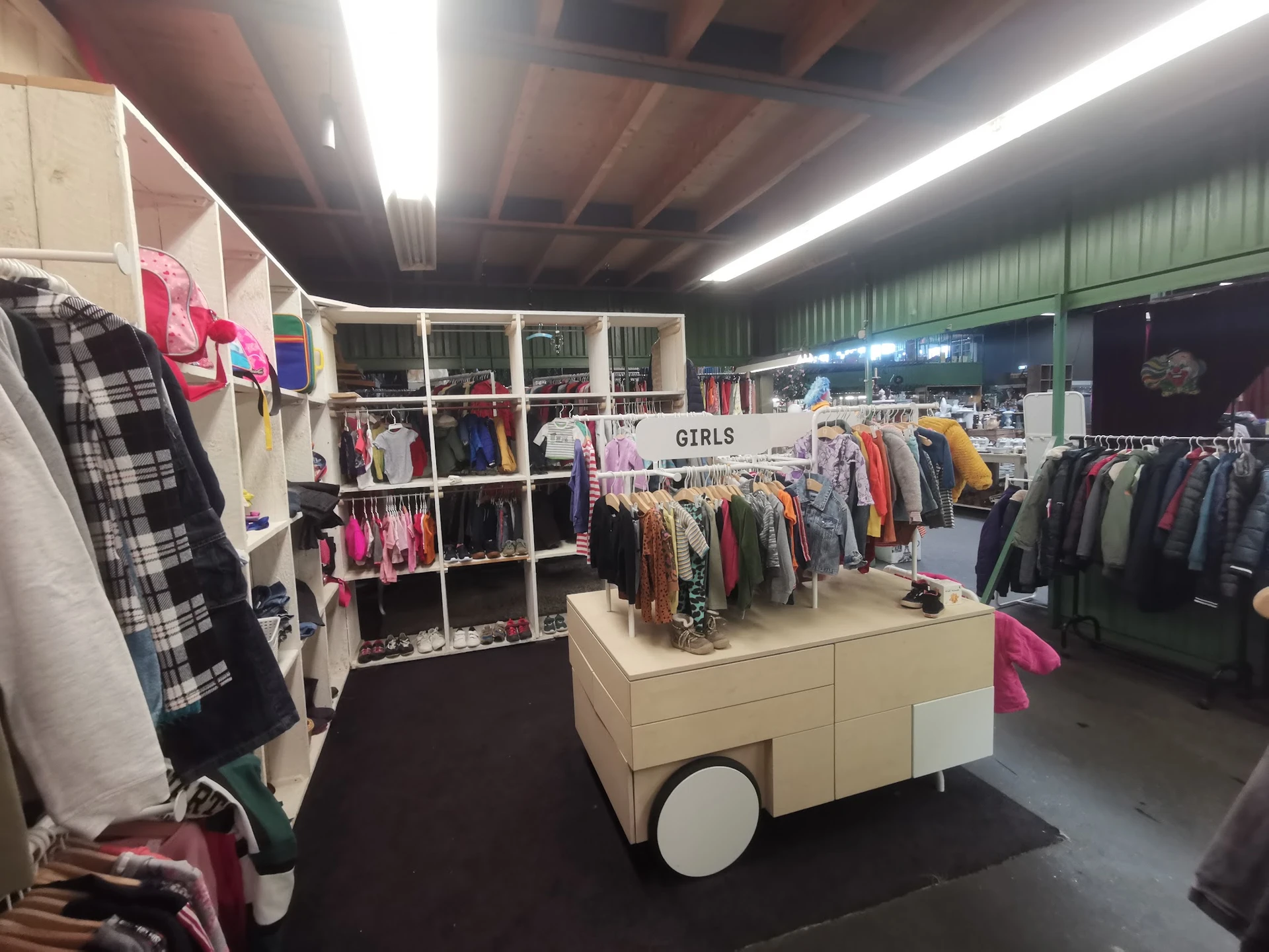 Winkelvloer met kledingrekken en stellingen vol tweedehands kleding, onder andere een afdeling voor meisjeskleding