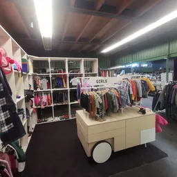 Winkelvloer met kledingrekken en stellingen vol tweedehands kleding, onder andere een afdeling voor meisjeskleding