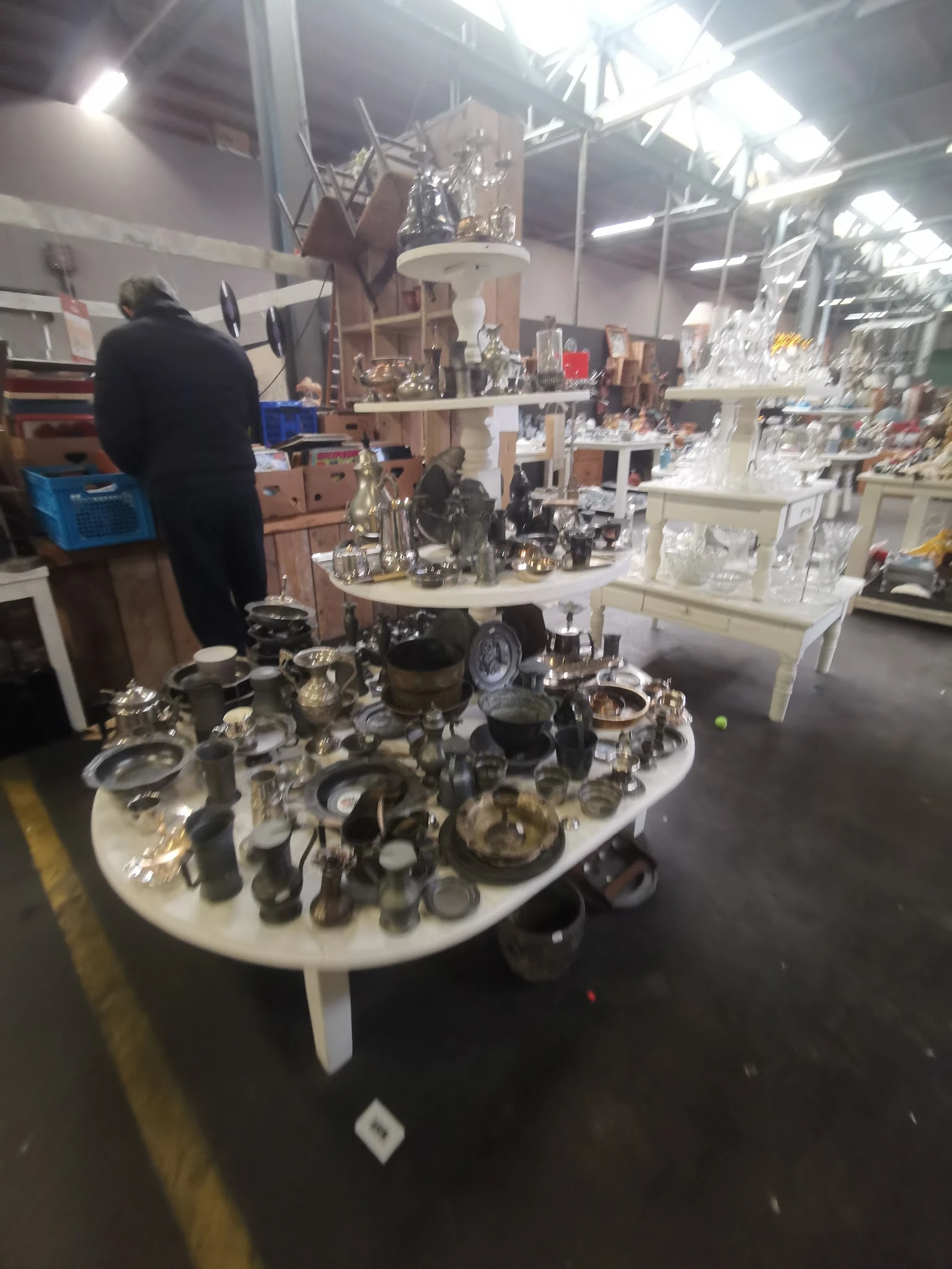 Tafel vol zilveren en metalen huishoudartikelen, servies en decoratievoorwerpen in een kringloopwinkel