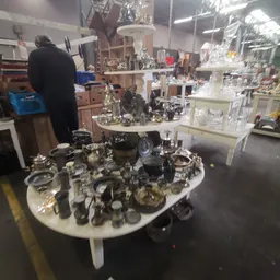 Tafel vol zilveren en metalen huishoudartikelen, servies en decoratievoorwerpen in een kringloopwinkel
